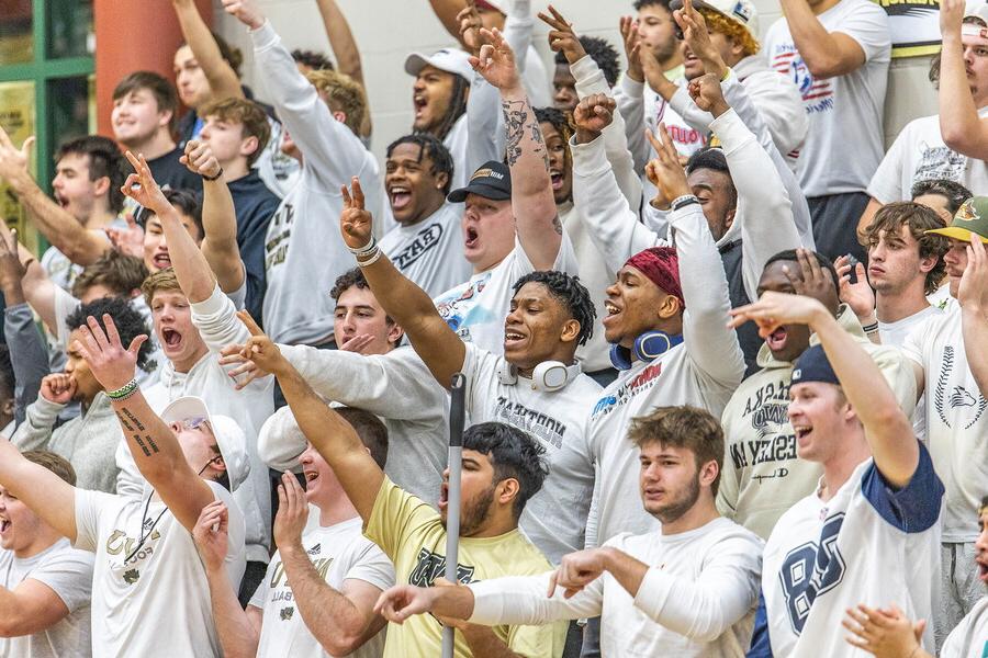 Basketball stands full of students with hands in the air cheering.